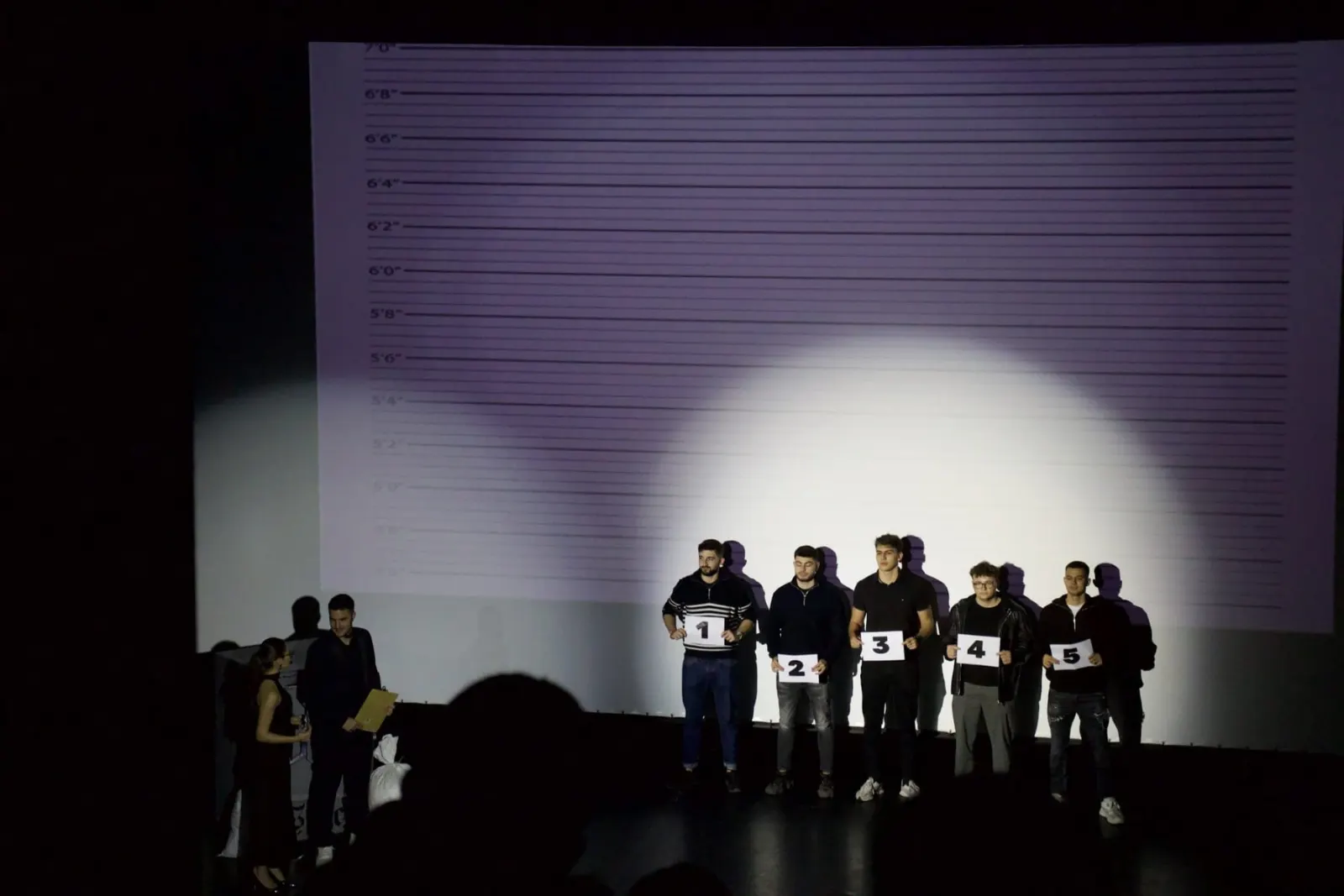 Five finalists lined up on stage under a spotlight