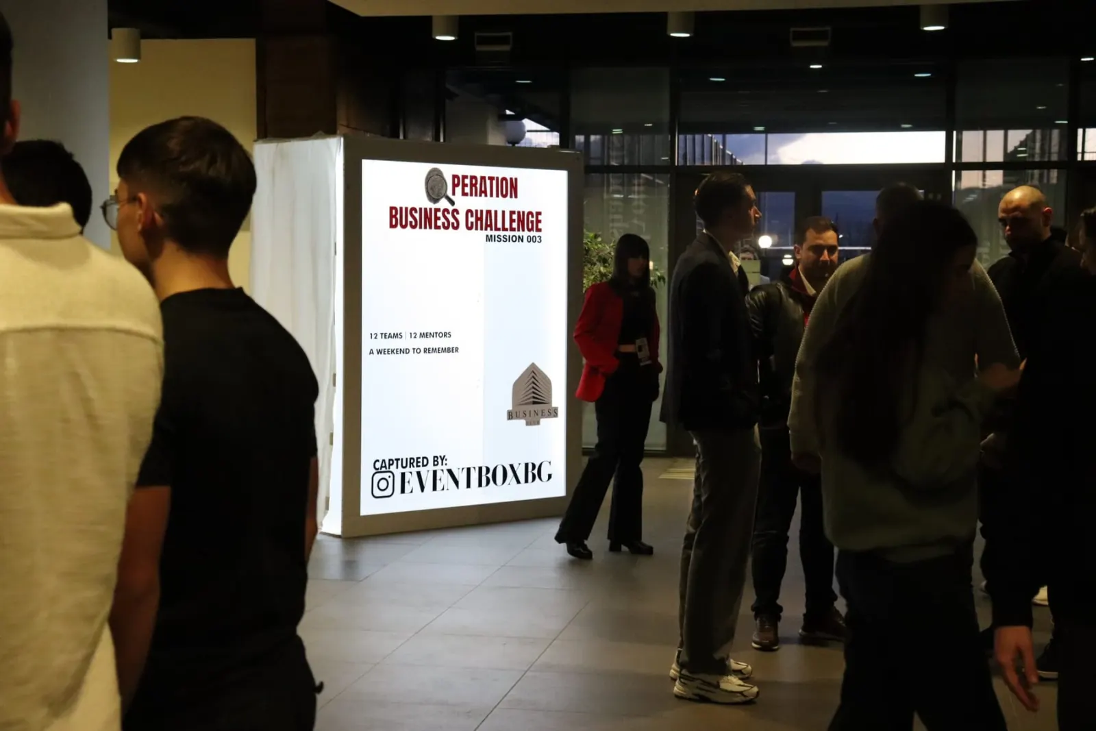 Guests gathering in the lobby next to the Operation Business Challenge poster